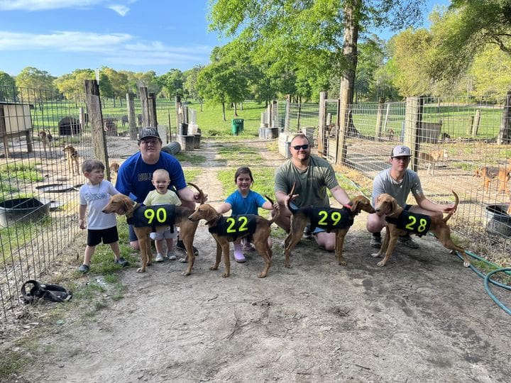 A group of people with dogs in the dirt.