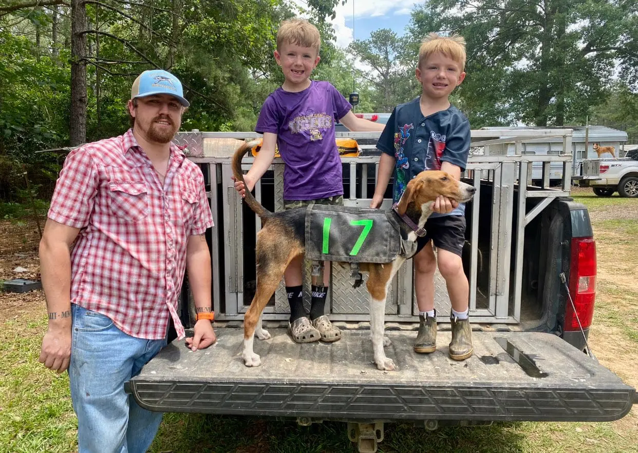 A man and two boys with a dog on the back of a truck.