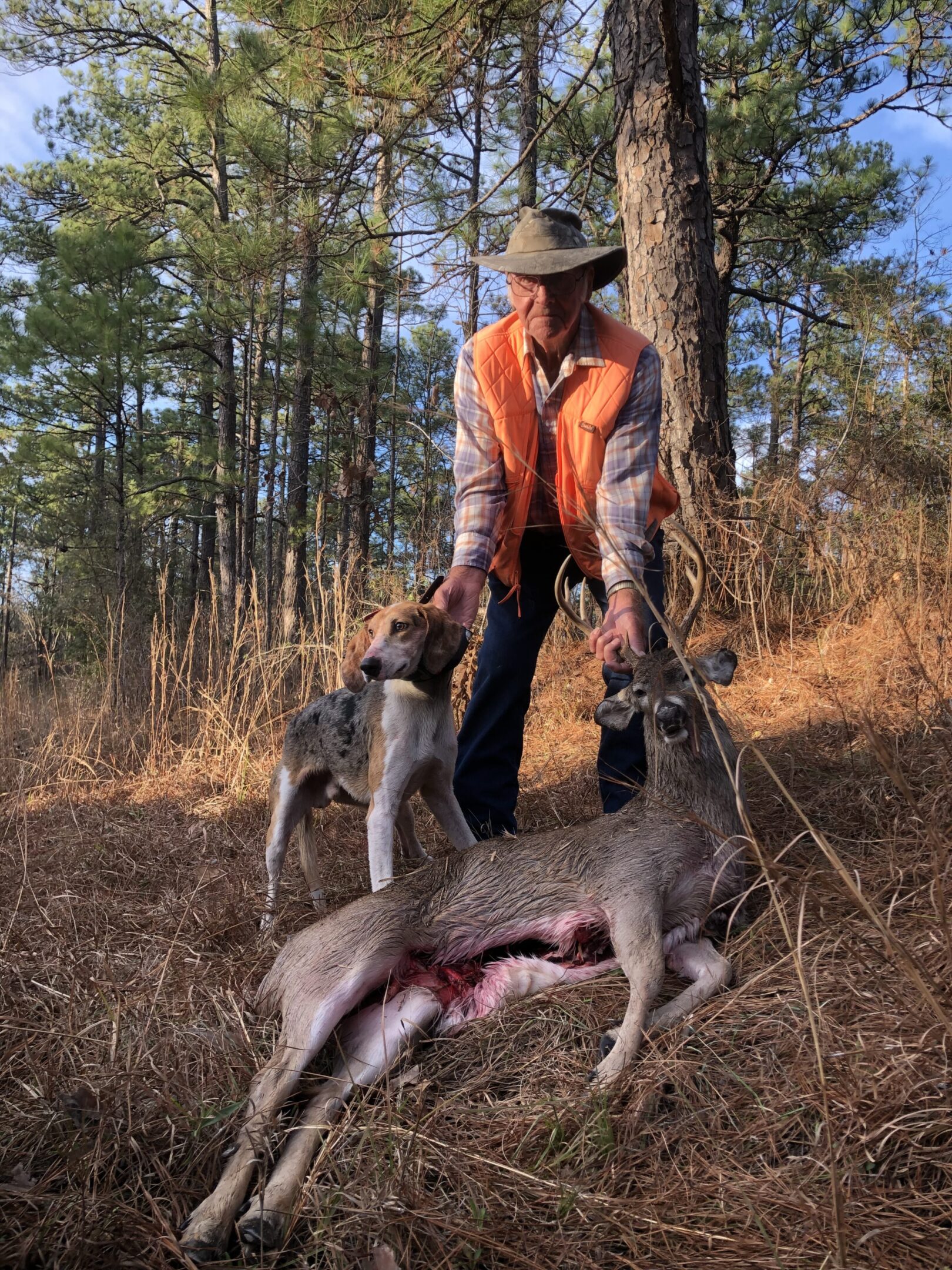 A man in an orange jacket holding two animals.